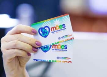 Mão de mulher segurando o Cartão Mães de Pernambuco, símbolo do programa social que abriu 2.654 vagas para auxílio de R$ 300 mensais.