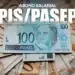Nota de 100 reais destacada sobre outras cédulas, ilustrando o abono salarial PIS/PASEP 2026.