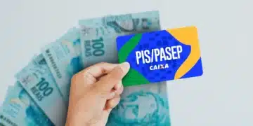 Mão segurando cartão PIS/PASEP com várias notas de 100 reais ao fundo em superfície branca