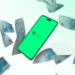 Smartphone exibindo o logotipo do Pix em uma tela verde, cercado por notas de 100 reais flutuando, representando transações financeiras e impostos.