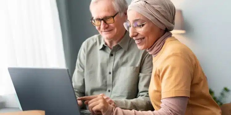Mulher árabe ajudando homem idoso a usar laptop em ambiente doméstico, simbolizando o suporte necessário para realizar a comprovação anual de benefícios previdenciários