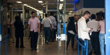 Pessoas em uma agência bancária ou ambiente de atendimento, algumas em fila, outras aguardando, representando a busca por soluções financeiras.