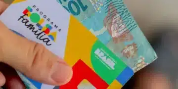 Cartão do Programa Bolsa Família com cédula de R$ 100,00 sendo segurada, representando o pagamento do benefício social.
