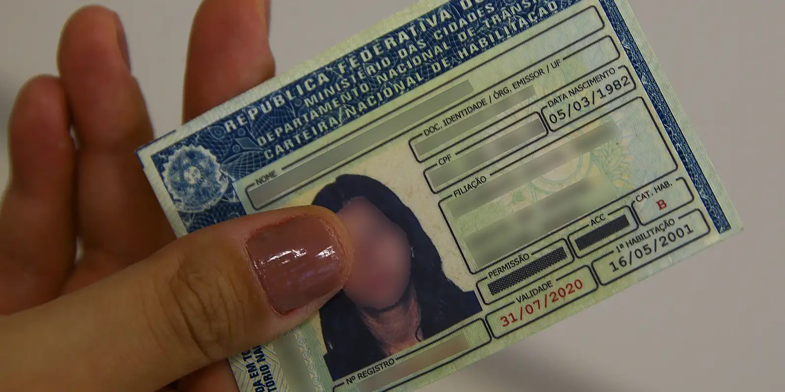Mão segurando a Carteira Nacional de Habilitação (CNH) no modelo físico, representando a documentação que poderá ser obtida sem autoescola se a nova proposta for aprovada.