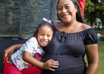Mãe abraça a filha pequena enquanto coloca a mão na barriga de gestante, simbolizando as beneficiárias do Programa Mães de Pernambuco.