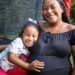 Mãe abraça a filha pequena enquanto coloca a mão na barriga de gestante, simbolizando as beneficiárias do Programa Mães de Pernambuco.