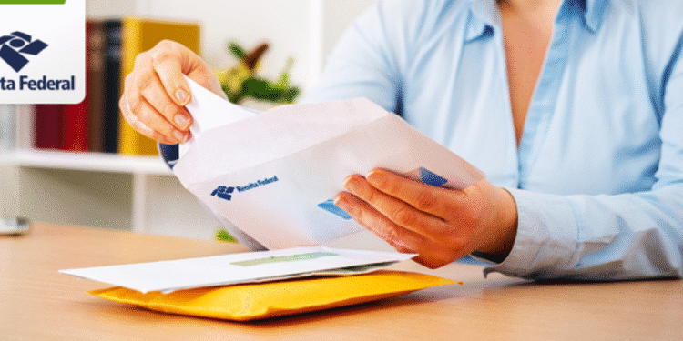 Uma pessoa com camisa azul abrindo cuidadosamente um envelope branco com o logotipo da Receita Federal em uma mesa de escritório. A imagem ilustra o momento de recebimento de uma comunicação oficial.