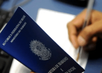 Carteira de trabalho sendo segurada por uma pessoa enquanto assina um documento.