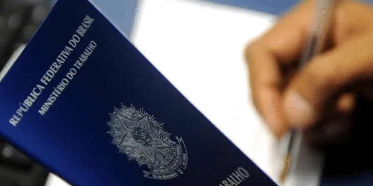 Carteira de trabalho sendo segurada por uma pessoa enquanto assina um documento.