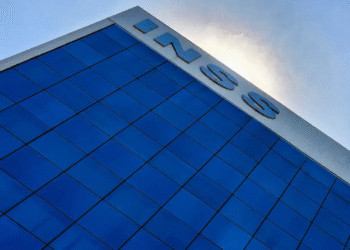 Fachada de prédio com o logo do INSS em destaque, sob céu azul, representando a instituição