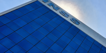 Fachada de prédio com o logo do INSS em destaque, sob céu azul, representando a instituição