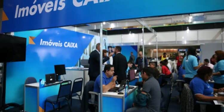 Estande de atendimento da Caixa Econômica Federal em evento, com a placa "Imóveis CAIXA" e funcionários conversando com clientes.