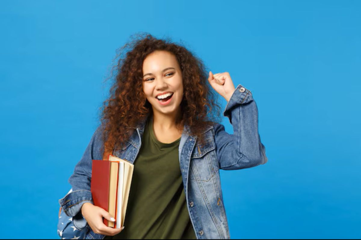 Estudante Elegível para Benefício Estudante jovem, com cabelo cacheado e livros, celebra com o punho erguido, representando elegibilidade para benefício.