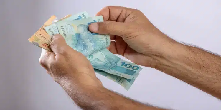 Saque calamidade do FGTS: veja quem pode solicitar o dinheiro a partir desta quarta-feira (14/10) 1 Mãos de uma pessoa contando cédulas de reais, ilustrando a liberação do Saque Calamidade do FGTS