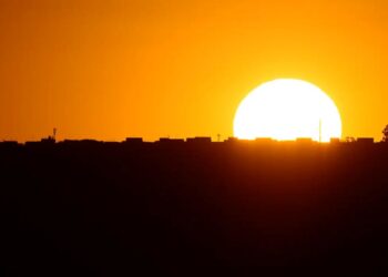 Pôr do sol alaranjado sobre a silhueta da cidade, representando a mudança de horário causada pela decisão do Governo sobre o Horário de Verão 2025.