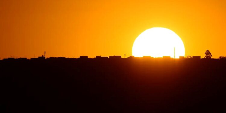 Pôr do sol alaranjado sobre a silhueta da cidade, representando a mudança de horário causada pela decisão do Governo sobre o Horário de Verão 2025.