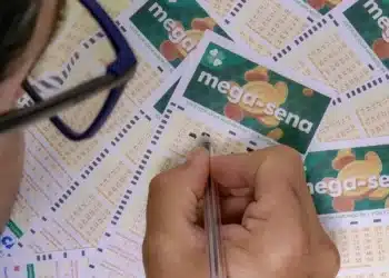 Pessoa preenchendo cartão da Mega-Sena com caneta sobre várias apostas.