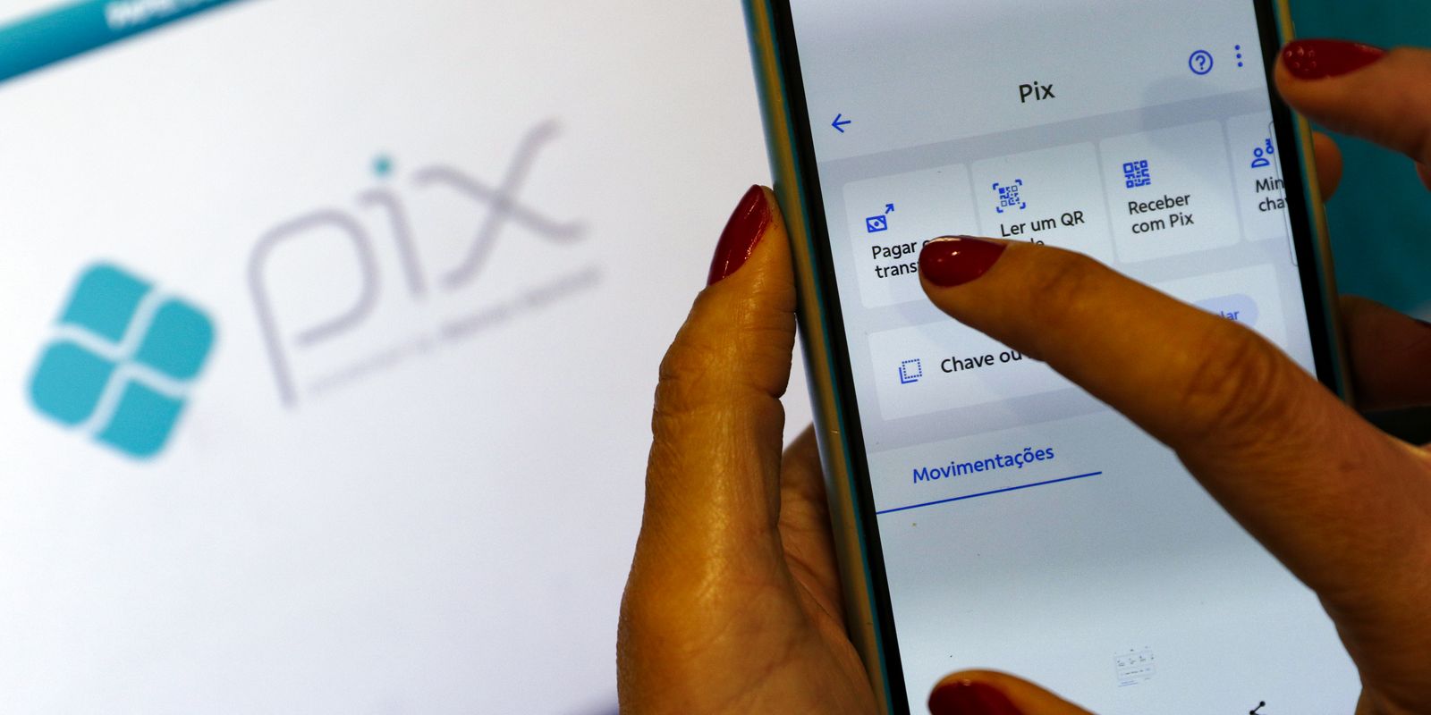 Mãos utilizando um smartphone com o aplicativo do Pix, com a logo do Pix ao fundo.