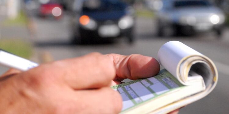 Agente de trânsito anotando uma infração em um bloco de multas durante fiscalização.