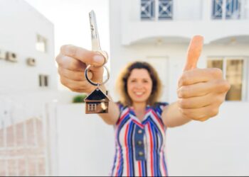Mulher segurando chaves de uma casa nova e fazendo sinal de positivo, simbolizando a conquista da casa própria.