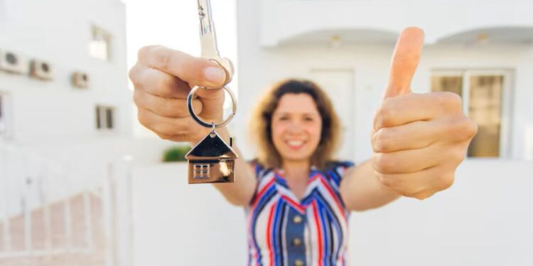 Mulher segurando chaves de uma casa nova e fazendo sinal de positivo, simbolizando a conquista da casa própria.