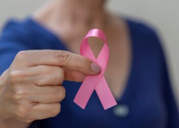 Fita rosa símbolo do Outubro Rosa em foco, segurada por uma mulher, representando a conscientização sobre o câncer e os direitos dos pacientes.