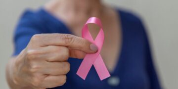 Fita rosa símbolo do Outubro Rosa em foco, segurada por uma mulher, representando a conscientização sobre o câncer e os direitos dos pacientes.