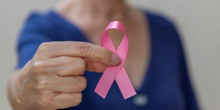 Fita rosa símbolo do Outubro Rosa em foco, segurada por uma mulher, representando a conscientização sobre o câncer e os direitos dos pacientes.