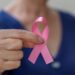 Fita rosa símbolo do Outubro Rosa em foco, segurada por uma mulher, representando a conscientização sobre o câncer e os direitos dos pacientes.