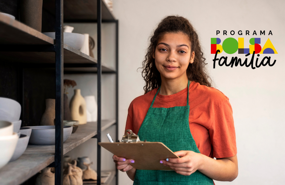 Mulher sorrindo e segurando uma prancheta, em um ambiente de trabalho com prateleiras de cerâmica ao fundo. Representa uma situação de inclusão social com o auxílio do Bolsa Família.