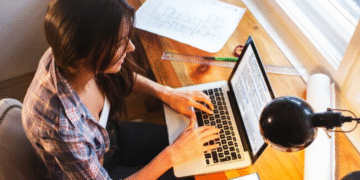 Mulher trabalhando em casa usando notebook sobre mesa de madeira