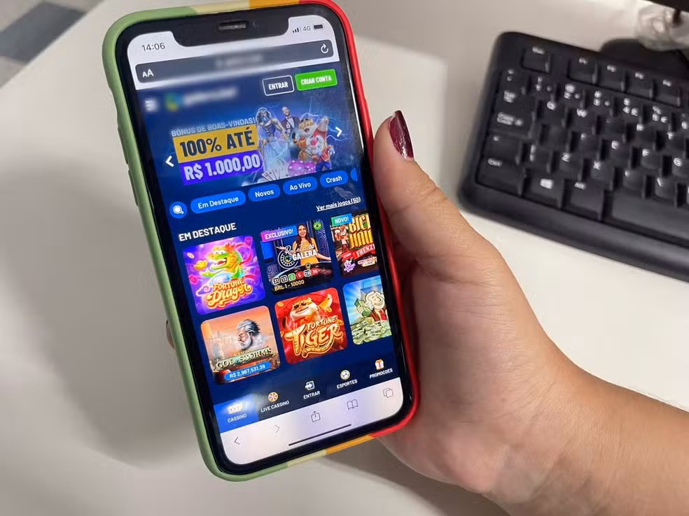 Smartphone exibindo um aplicativo de apostas online com ofertas de bônus e diversos jogos como "Fortune Dragon" e "Fortune Tiger" em destaque. A mão de uma pessoa segura o aparelho