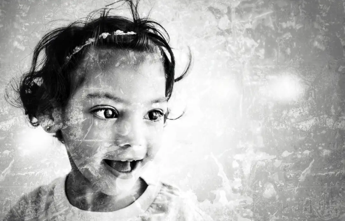 Foto em preto e branco de uma menina sorridente com faixa no cabelo e olhos grandes.