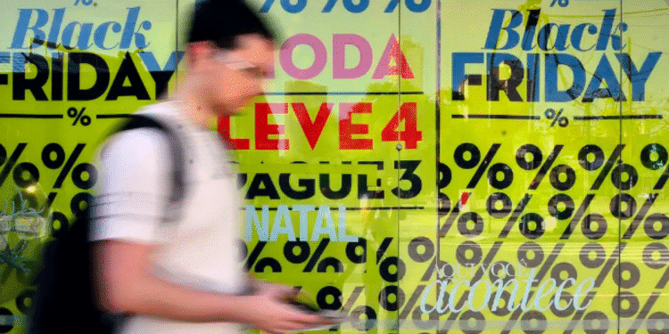 Pessoa caminhando com smartphone em frente a vitrine de loja com cartazes de promoções da Black Friday e descontos em porcentagem.