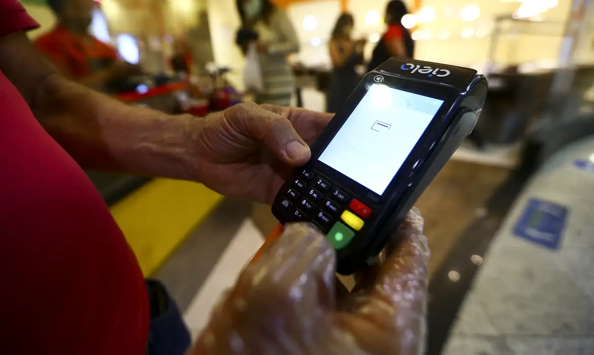 Taxa Máxima e Maquininhas: Entenda as Principais Mudanças nas Regras dos Vales em 2025 Trabalhador usando um cartão na maquininha Cielo, representando o pagamento e as novas regras do Governo sobre a aceitação e limite de taxas do vale-alimentação e vale-refeição.