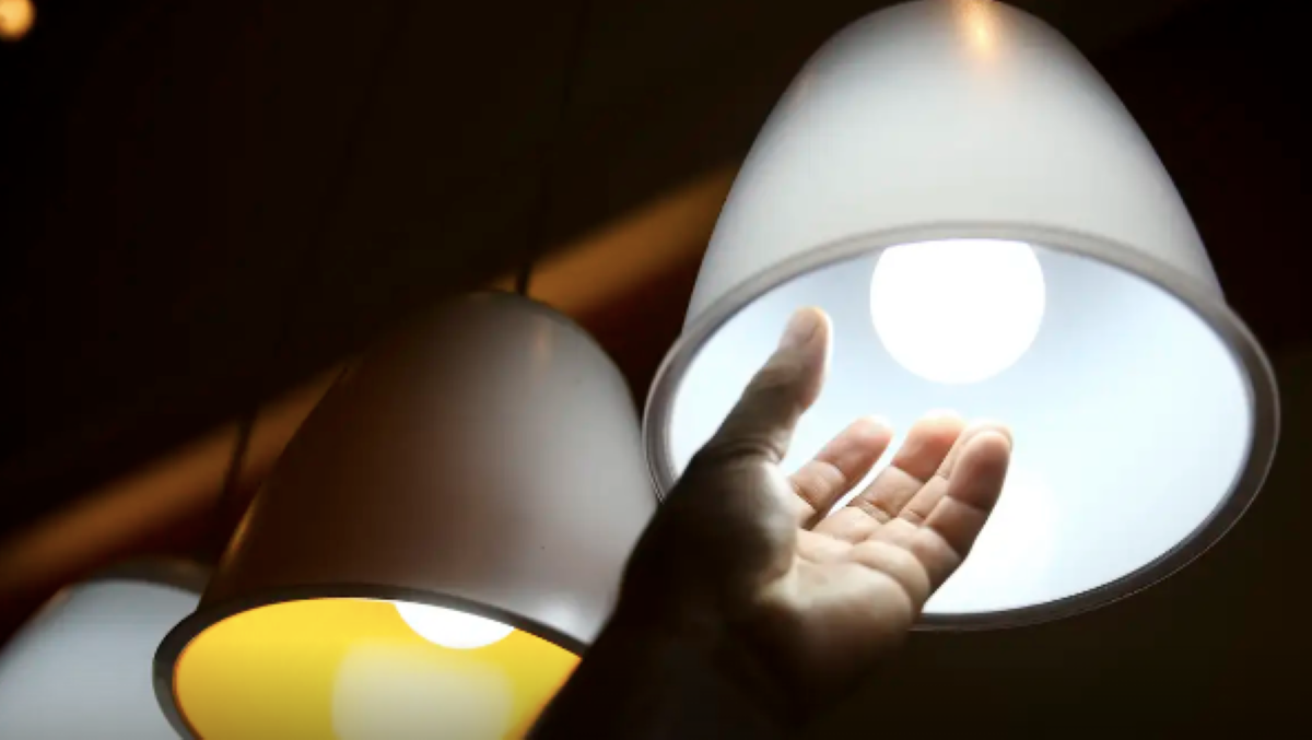 Imagem de uma mão tocando uma lâmpada acesa, simbolizando o acesso à energia elétrica gratuita pelo Cadastro Único.