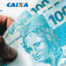 Mão segurando cédulas de 100 reais com logos do Banco do Brasil e da Caixa no fundo.