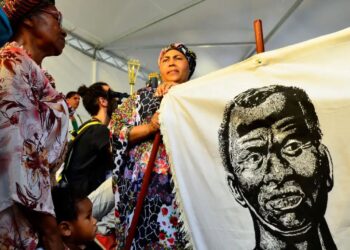 Pessoas celebrando o Dia da Consciência Negra em 20 de novembro, segurando um cartaz com imagem de figura histórica afro-brasileira, simbolizando a data do feriado.