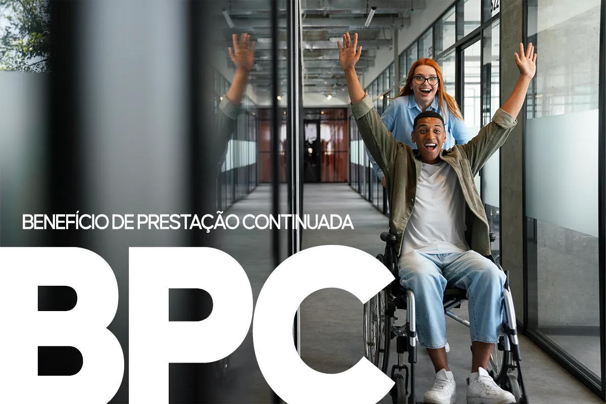 Inclusão e Apoio Social pelo BPC Pessoa em cadeira de rodas com os braços erguidos em sinal de celebração, sendo empurrada por uma mulher em ambiente corporativo. A imagem representa a superação e a inclusão social facilitada pelo Benefício de Prestação Continuada (BPC).