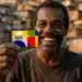 Homem negro sorridente segura cartão colorido do Programa Bolsa Família em área urbana ao fundo