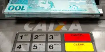 Pilha de cédulas de 100 reais saindo de caixa eletrônico da Caixa Econômica com teclado colorido iluminado