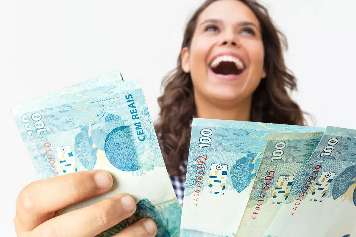Mulher feliz segurando cédulas de cem reais Mulher sorridente segurando várias cédulas de cem reais em ambas as mãos