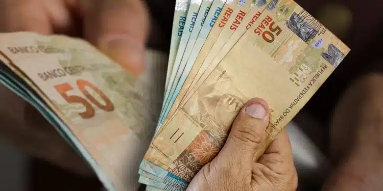 Mãos contando notas de dinheiro, simbolizando o recebimento da primeira parcela do 13º salário.