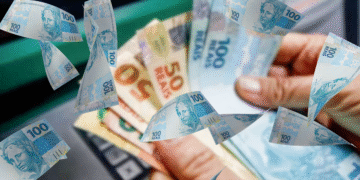 Mão segurando notas de 100 e 50 reais com notas de 100 flutuando. Representação de dinheiro, salário e décimo terceiro pagamento.