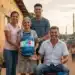 Família de diferentes gerações em comunidade, sorrindo e segurando um botijão "Gás do Povo", simbolizando o impacto dos programas Luz do Povo e Gás do Povo.