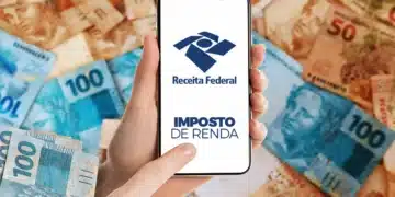 Mão segurando smartphone com o aplicativo da Receita Federal e a inscrição 'Imposto de Renda', cercado por notas de real, indicando consulta à restituição.