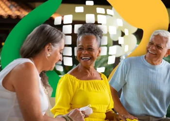 Três idosos sorridentes conversando alegremente em ambiente ao ar livre com fundo colorido e decoração moderna