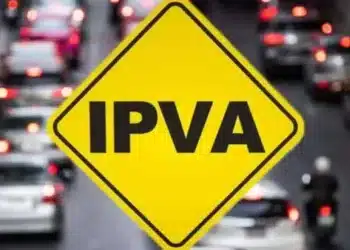 Placa amarela com a sigla IPVA em destaque sobre tráfego de carros em uma rua movimentada