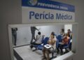 Interior de sala de espera para perícia médica do INSS, com várias pessoas aguardando atendimento, com foco em mulheres sentadas.