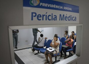 Interior de sala de espera para perícia médica do INSS, com várias pessoas aguardando atendimento, com foco em mulheres sentadas.